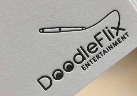 Close-up of a pen resting on a logo that reads 'DoodleFlix ENTERTAINMENT.'